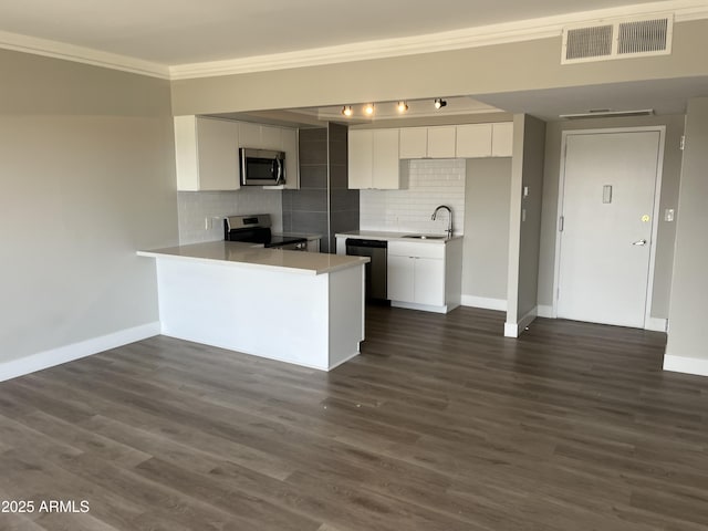 kitchen with appliances with stainless steel finishes, a peninsula, white cabinets, decorative backsplash, and baseboards