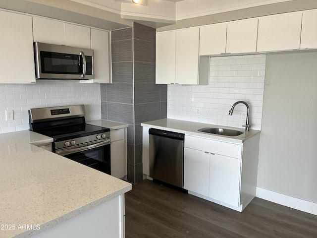 kitchen with appliances with stainless steel finishes, a sink, decorative backsplash, dark wood-style floors, and white cabinetry