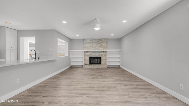 unfurnished living room featuring a sink, a fireplace, recessed lighting, baseboards, and light wood-type flooring