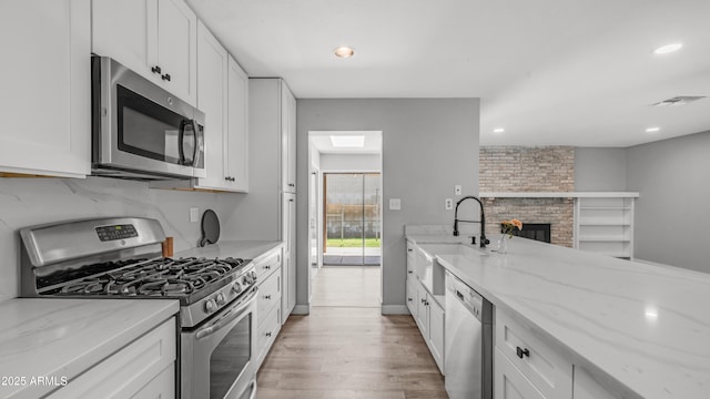 kitchen with light wood-style floors, a sink, light stone countertops, and stainless steel appliances