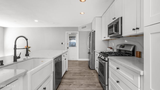 kitchen featuring white cabinets, a sink, light wood-style floors, stainless steel appliances, and visible vents