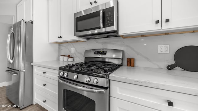 kitchen with wood finished floors, white cabinets, light stone counters, appliances with stainless steel finishes, and backsplash
