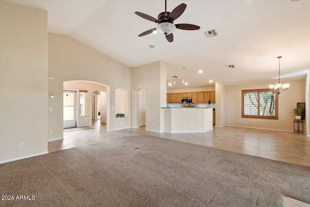 unfurnished living room featuring ceiling fan with notable chandelier, light colored carpet, high vaulted ceiling, and plenty of natural light