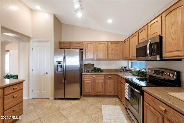 kitchen with light stone counters, light tile patterned floors, stainless steel appliances, and vaulted ceiling