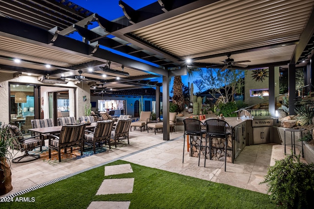 patio at night featuring ceiling fan, an outdoor living space, exterior bar, grilling area, and an outdoor kitchen