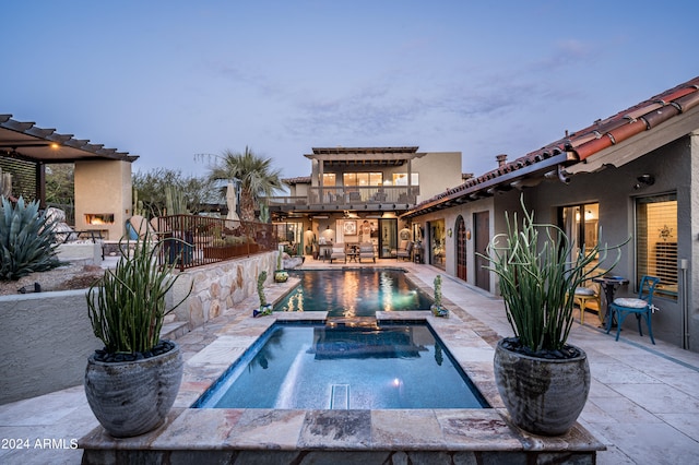 pool at dusk featuring exterior fireplace, a patio area, and an in ground hot tub