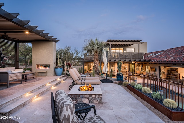 patio terrace at dusk with an outdoor fire pit, a balcony, and an outdoor stone fireplace