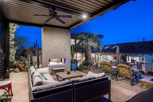 patio terrace at dusk with ceiling fan and an outdoor living space with a fireplace