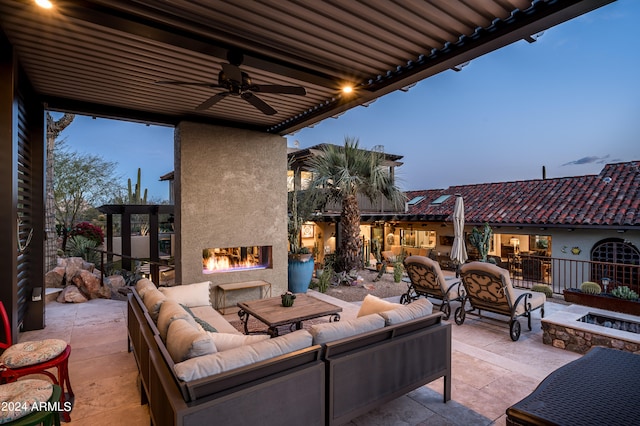 patio terrace at dusk with ceiling fan and an outdoor living space with a fireplace