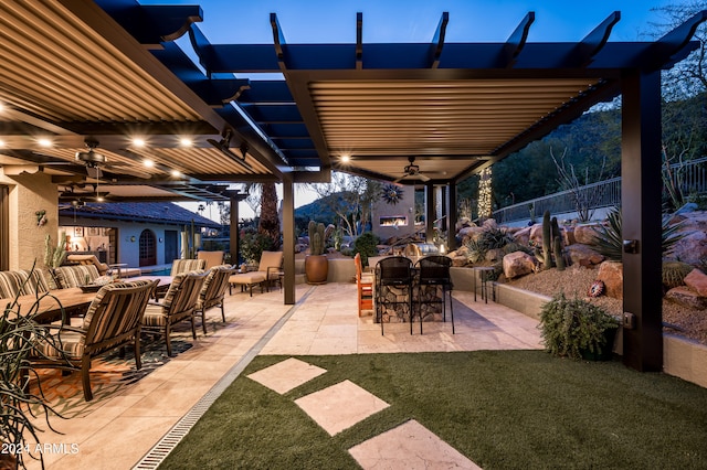 patio terrace at dusk with ceiling fan, an outdoor bar, a yard, and an outdoor living space