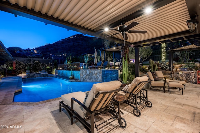 pool at dusk with ceiling fan, a patio area, and a mountain view