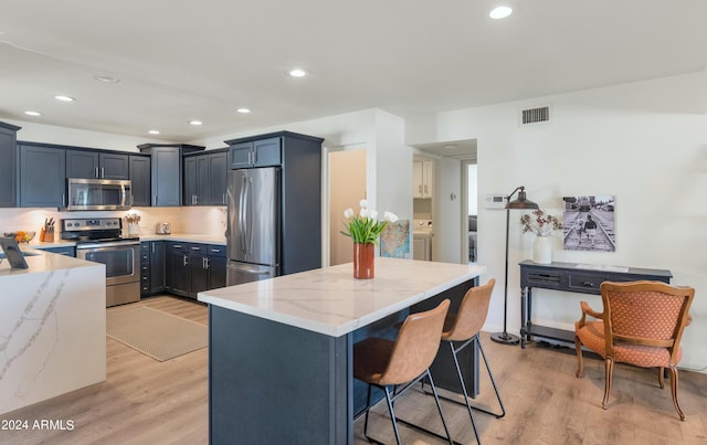 kitchen featuring a kitchen breakfast bar, appliances with stainless steel finishes, light hardwood / wood-style floors, light stone counters, and washer / clothes dryer