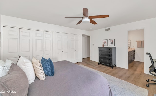 bedroom with light hardwood / wood-style floors, ensuite bath, ceiling fan, and multiple closets