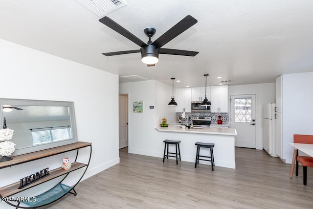 kitchen with a breakfast bar area, white cabinets, hanging light fixtures, kitchen peninsula, and stainless steel appliances