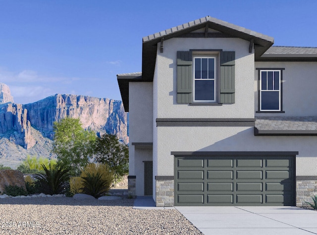 view of front of house with stucco siding, driveway, stone siding, a mountain view, and an attached garage