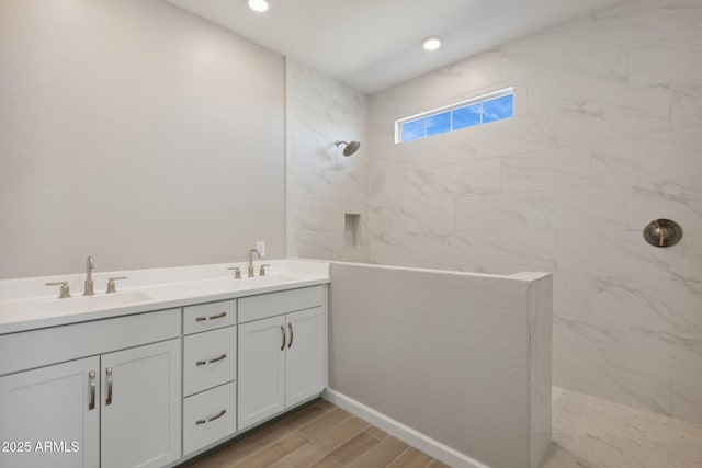 bathroom featuring a sink, tiled shower, double vanity, and wood finish floors