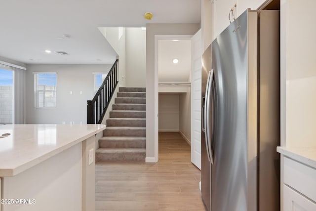 interior space with light wood finished floors, visible vents, light stone countertops, stainless steel fridge with ice dispenser, and white cabinetry