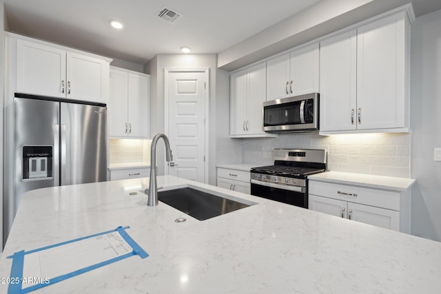 kitchen with a sink, light stone countertops, backsplash, and appliances with stainless steel finishes