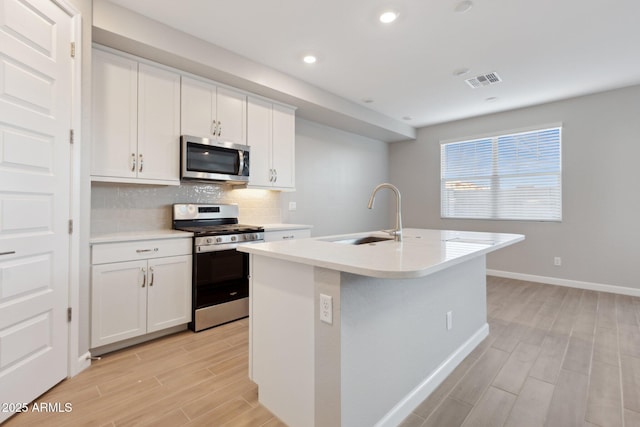 kitchen featuring visible vents, wood finish floors, a sink, decorative backsplash, and stainless steel appliances