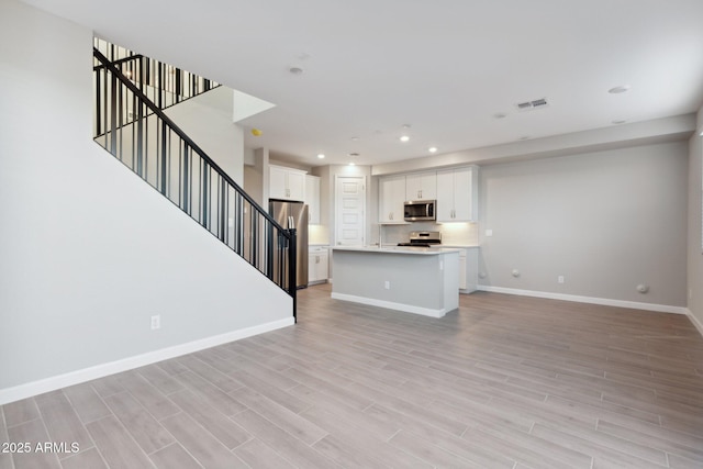 unfurnished living room featuring stairway, visible vents, baseboards, recessed lighting, and light wood-style floors