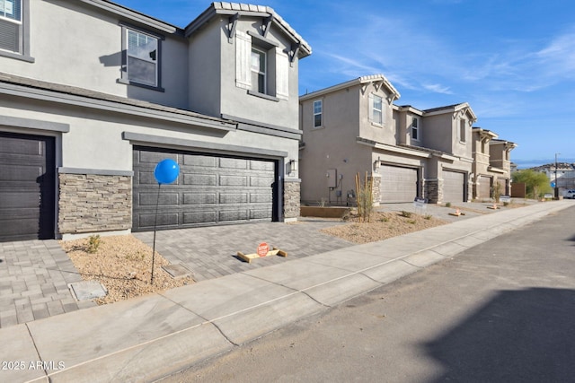 view of front of house with stucco siding, a garage, stone siding, decorative driveway, and a residential view