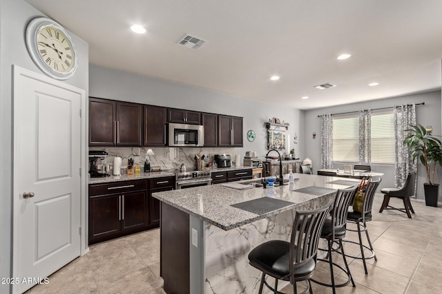 kitchen featuring sink, a breakfast bar area, a kitchen island with sink, stainless steel appliances, and light stone countertops