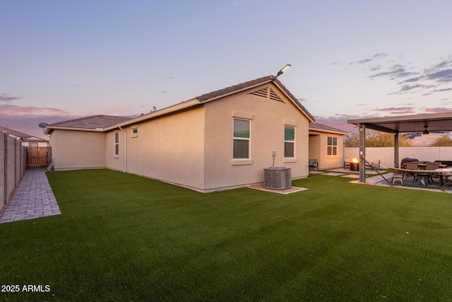 back house at dusk with a patio, central AC unit, and a lawn