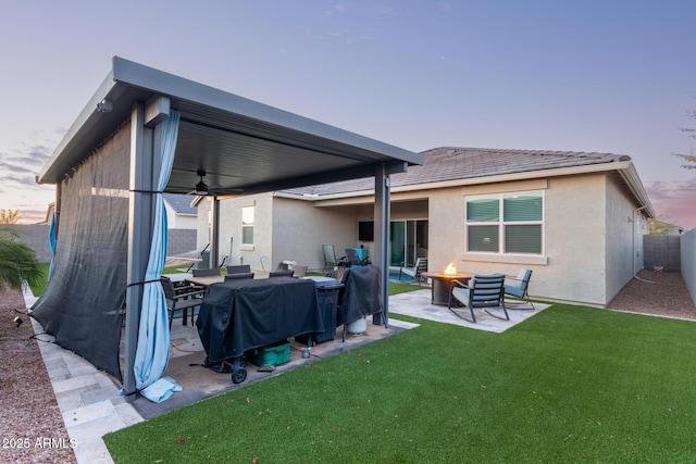 back house at dusk with ceiling fan, an outdoor fire pit, a patio area, and a lawn