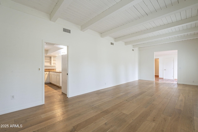 empty room featuring visible vents, beamed ceiling, light wood-type flooring, and baseboards