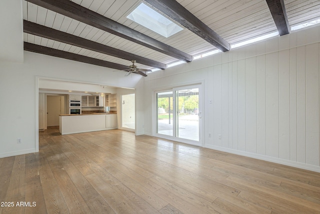 unfurnished living room featuring beam ceiling, light wood-style flooring, a ceiling fan, a skylight, and baseboards