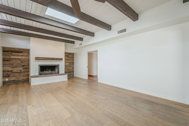 unfurnished living room with visible vents, a fireplace with raised hearth, a skylight, light wood finished floors, and baseboards