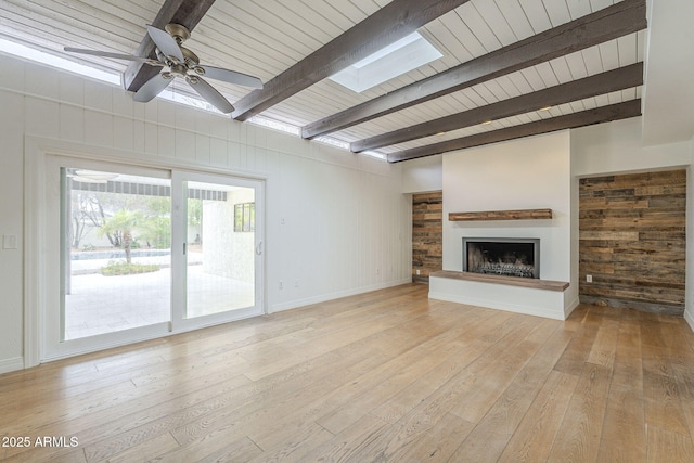 unfurnished living room with light wood-type flooring, beam ceiling, a fireplace with raised hearth, a skylight, and ceiling fan