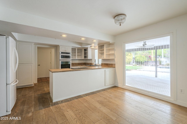 kitchen with multiple ovens, open shelves, wood finished floors, freestanding refrigerator, and a peninsula