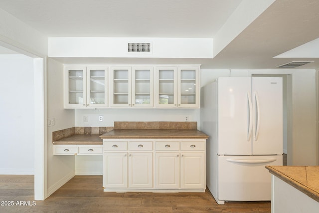 kitchen featuring visible vents, glass insert cabinets, wood finished floors, and freestanding refrigerator