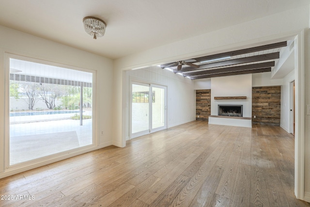 unfurnished living room with a fireplace with raised hearth, baseboards, beamed ceiling, a ceiling fan, and wood-type flooring