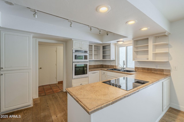 kitchen with wood finished floors, open shelves, a peninsula, a sink, and white double oven