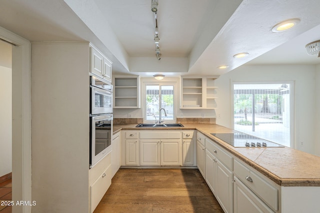 kitchen featuring wood finished floors, open shelves, a peninsula, a sink, and black electric stovetop