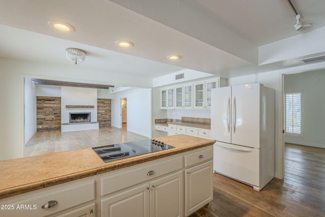 kitchen featuring visible vents, glass insert cabinets, hardwood / wood-style floors, freestanding refrigerator, and black electric cooktop