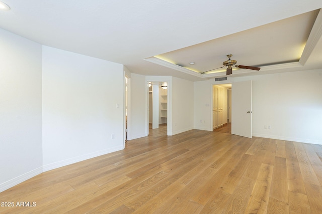 spare room featuring ceiling fan, baseboards, a raised ceiling, and light wood-style flooring