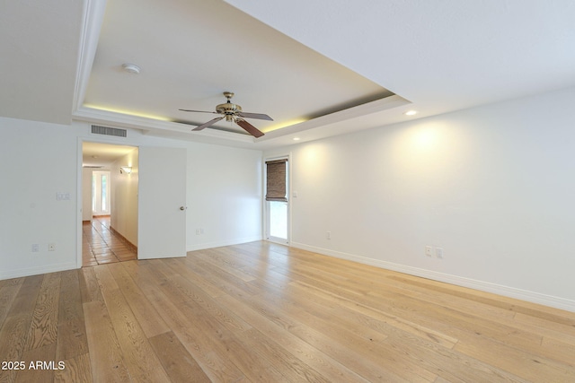 unfurnished room with a raised ceiling, plenty of natural light, light wood-style floors, and baseboards