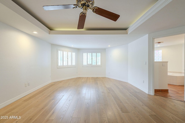 empty room featuring light wood-type flooring, a tray ceiling, baseboards, and a ceiling fan