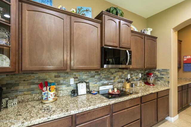 kitchen with black electric cooktop, light tile patterned flooring, light stone countertops, and backsplash