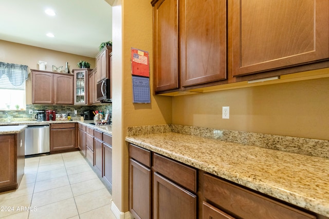 kitchen with appliances with stainless steel finishes, light tile patterned floors, tasteful backsplash, and light stone counters