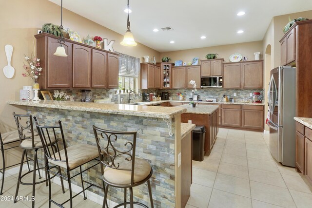 kitchen with appliances with stainless steel finishes, tasteful backsplash, light stone counters, kitchen peninsula, and decorative light fixtures