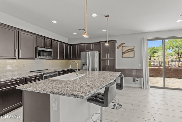 kitchen featuring light stone counters, stainless steel appliances, sink, pendant lighting, and a kitchen island with sink