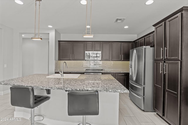 kitchen featuring light stone countertops, pendant lighting, a kitchen island with sink, stainless steel appliances, and sink