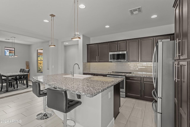 kitchen with a kitchen island with sink, a kitchen breakfast bar, light stone counters, sink, and appliances with stainless steel finishes