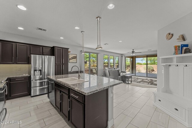 kitchen featuring light stone counters, stainless steel appliances, a kitchen island with sink, and sink