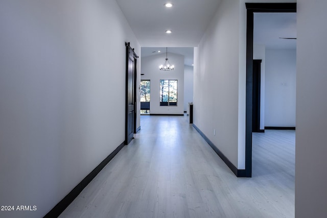 hallway featuring a barn door, light hardwood / wood-style flooring, lofted ceiling, and an inviting chandelier