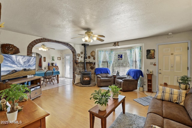 living room with ceiling fan, a wood stove, a textured ceiling, and light hardwood / wood-style floors